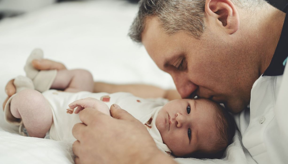 Mann mit grauen Schläfen küsst ein kleines Baby auf den Kopf.