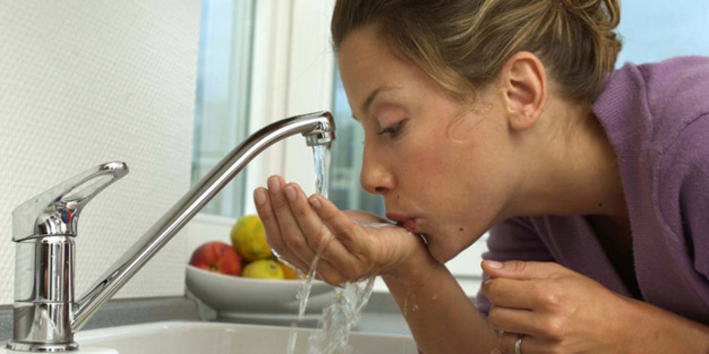 Frau trinkt aus dem Wasserhahn.