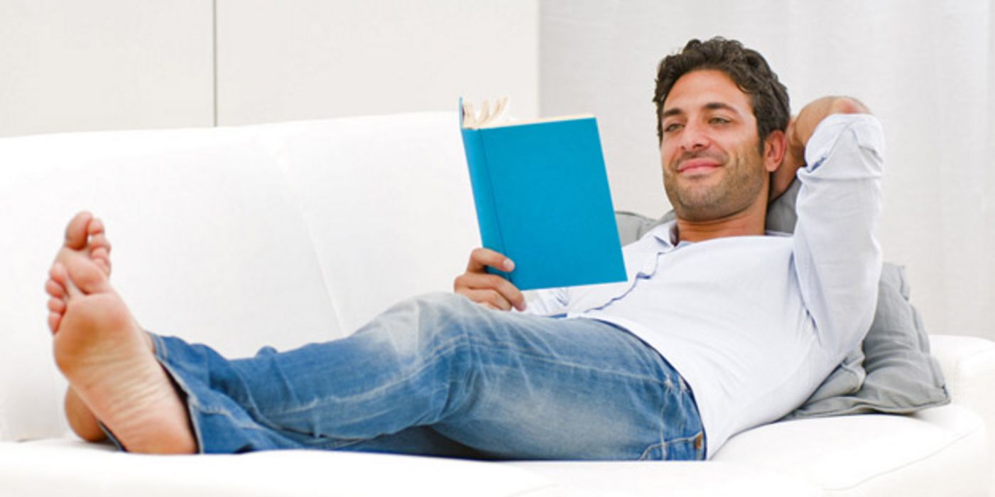 Junger Mann liegt entspannt auf einer Couch und liest