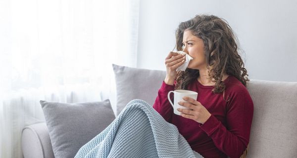 Erkältete Frau liegt auf dem Sofa und trinkt Tee.
