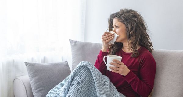 Erkältete Frau liegt auf dem Sofa und trinkt Tee.