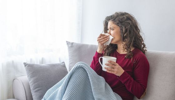 Erkältete Frau liegt auf dem Sofa und trinkt Tee.