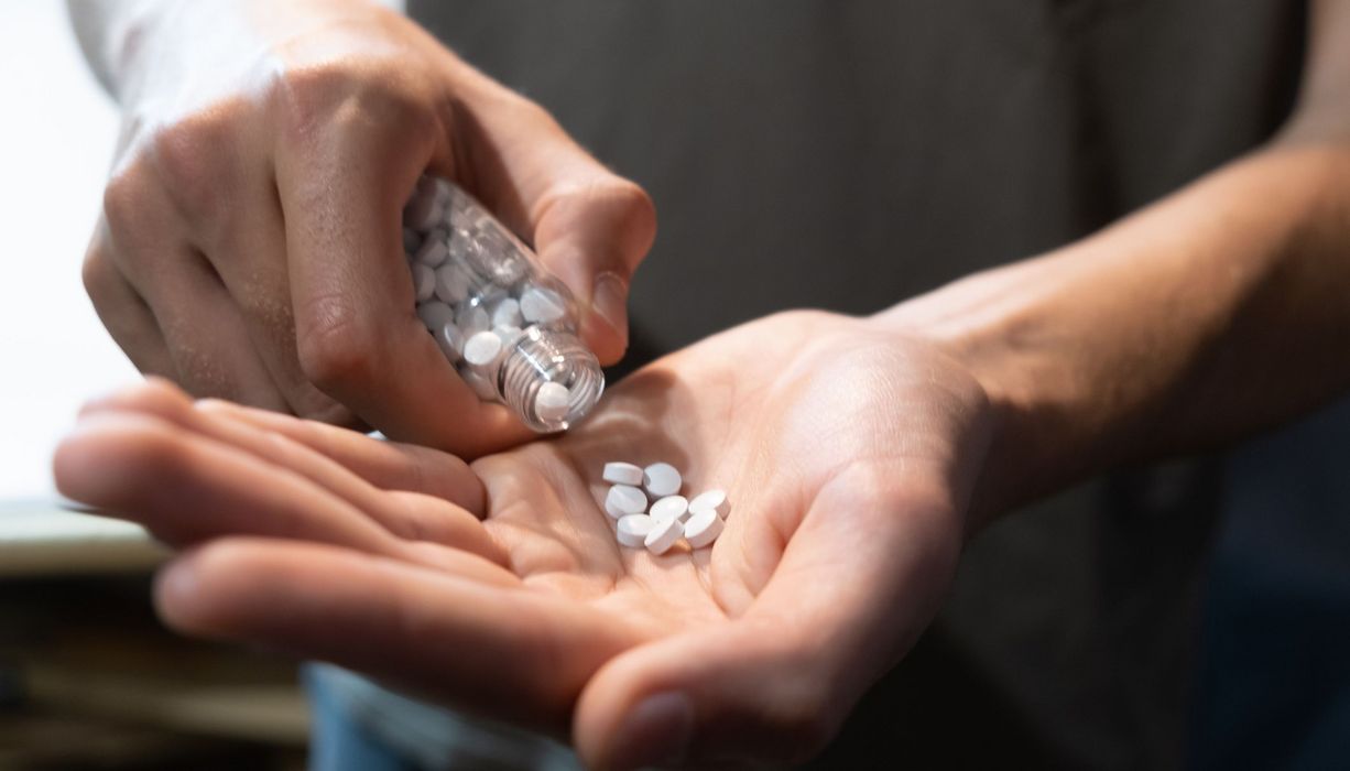 Mann, schüttet sich Tabletten in eine Hand.