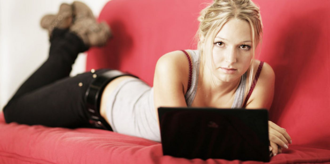 Junge Frau liegt auf einer Couch, vor ihr ein Laptop
