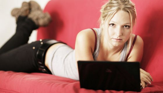 Junge Frau liegt auf einer Couch, vor ihr ein Laptop