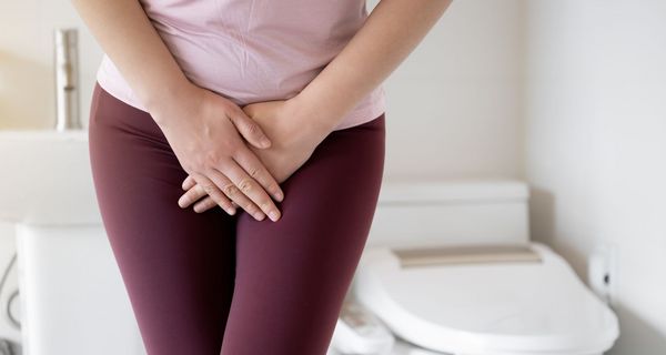 Frau hält sich den Unterleib, im Hintergrund ist eine Toilette zu erkennen.