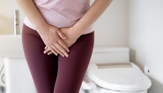 Frau hält sich den Unterleib, im Hintergrund ist eine Toilette zu erkennen.