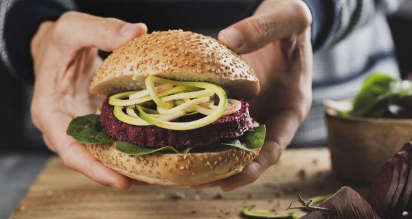 Zwei Hände halten einen pflanzlichen Burger.