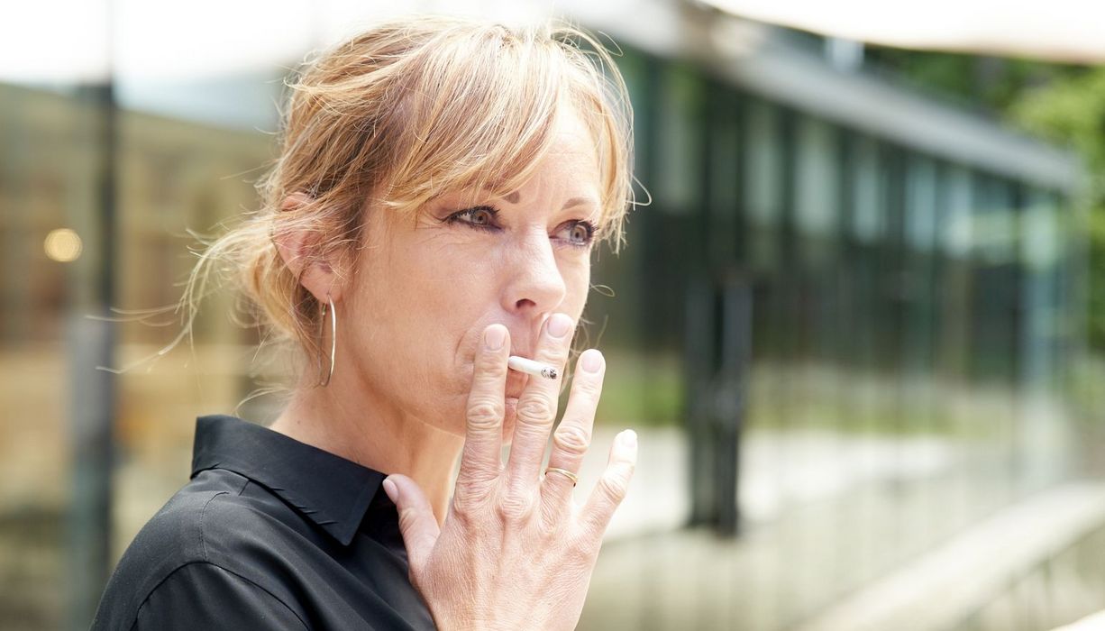 Eine Frau im Alter zwischen 30 und 45 Jahren raucht eine Zigarette.. 