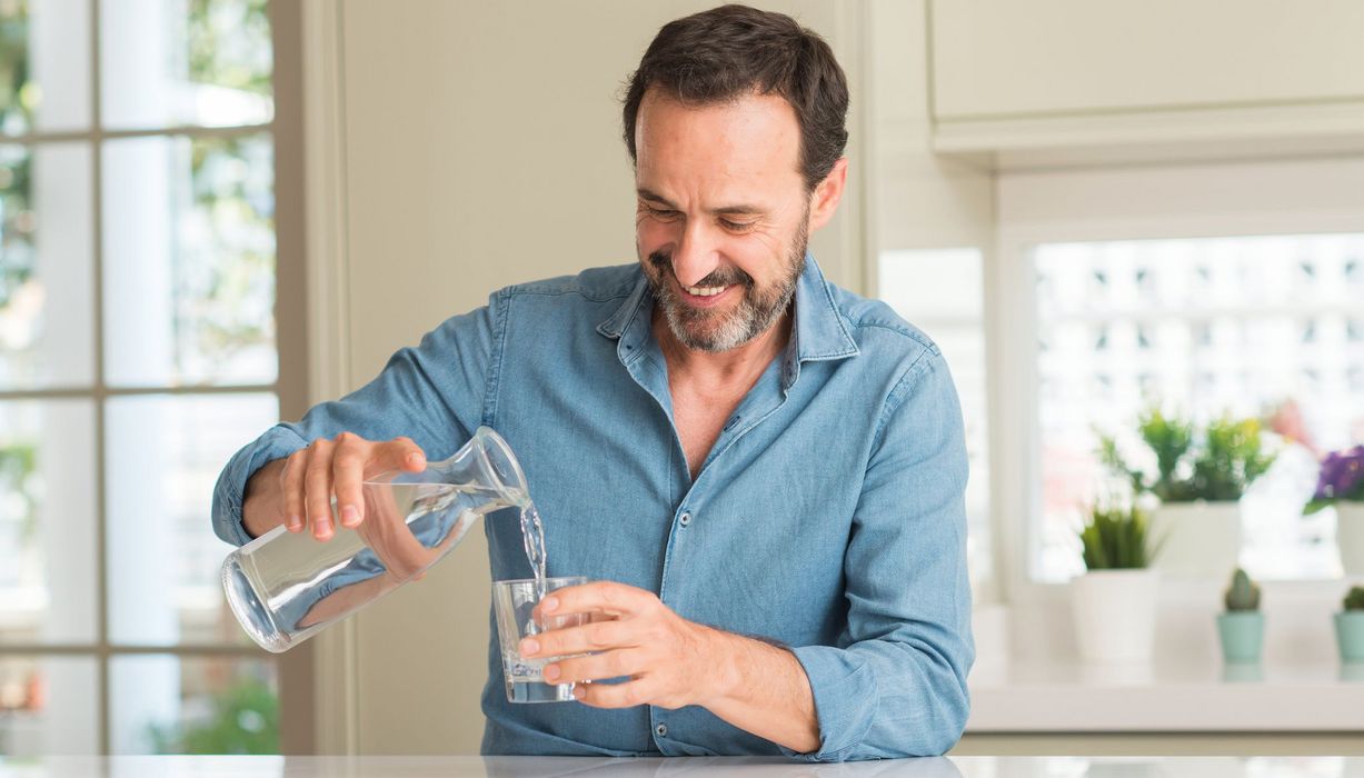Mann gießt sich ein Glas Wasser aus einer Glaskaraffe ein.