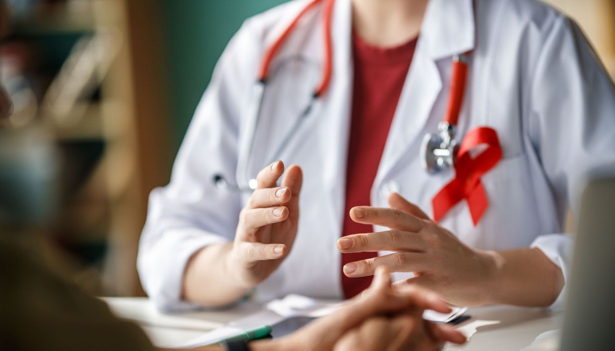 Eine Ärztin mit einer roten AIDS-Schleife spricht mit einem Patienten.