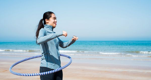 Frau am Strand mit Hula Hoop Reifen.