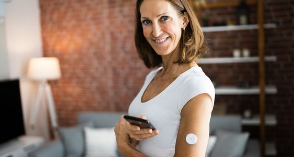 Ältere Frau mit einem Sensor für die kontinuierliche Blutzuckerüberwachung am Oberarm.