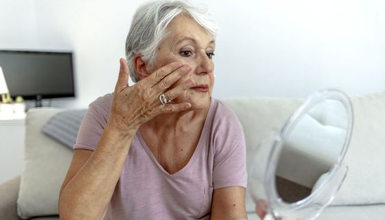 Frau, betrachtet ihr Gesicht in einem Handspiegel.
