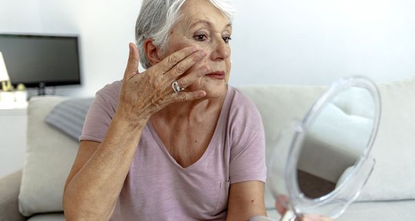 Frau, betrachtet ihr Gesicht in einem Handspiegel.