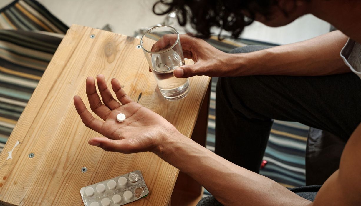 Mann, hält eine Tablette und ein Glas Wasser in der Hand.