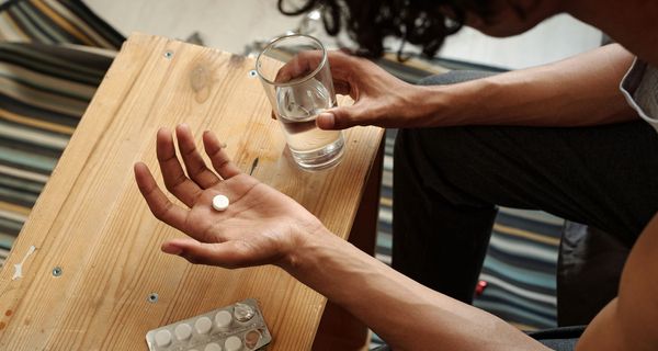 Mann, hält eine Tablette und ein Glas Wasser in der Hand.