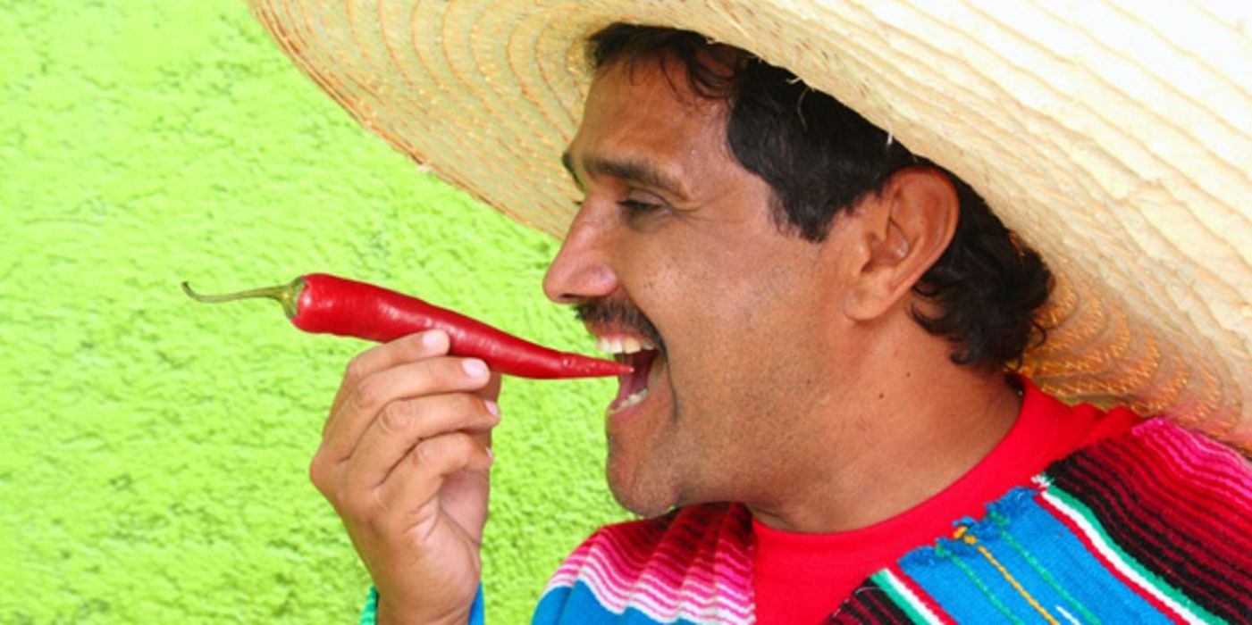 Mexikaner mit Sombrero beißt in Chili-Schote.