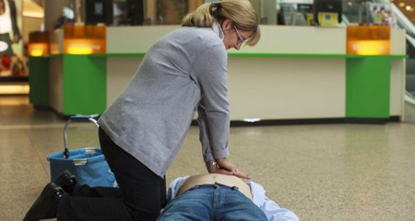 Frau führt Herzdruckmassage bei einem liegenden Mann durch.