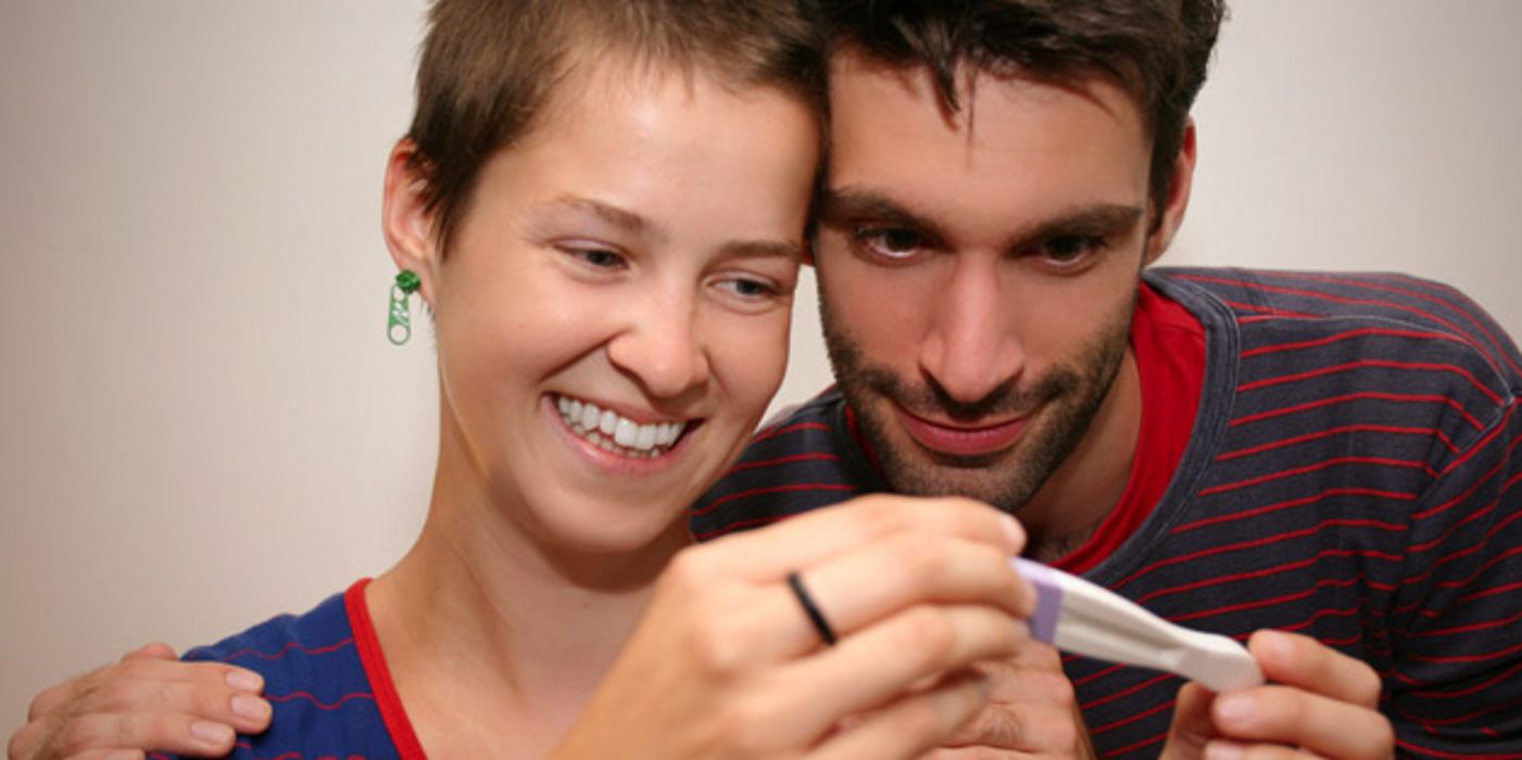 Junges Paar schaut gespannt auf einen Schwangerschaftstest.