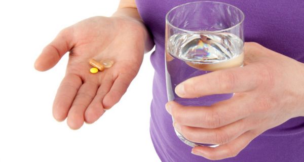 Zwei Hände, die Tabletten und ein Glas Wasser halten.