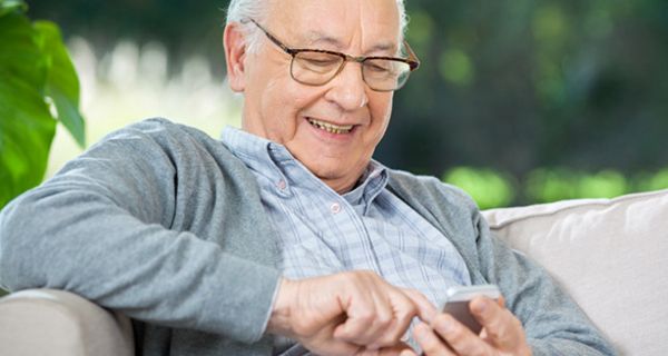 Senior mit Halbglatze auf Couch mit Smartphone