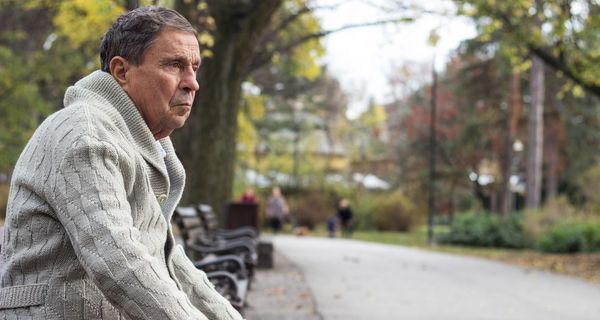Einsamer Senior sitzt im Park auf einer Bank und starrt in die Ferne.
