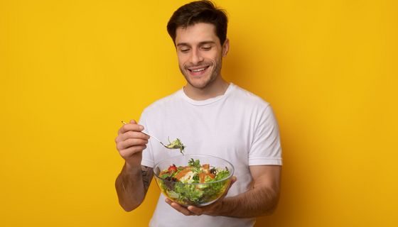 Ein Mann lächelt und hält eine Schüssel mit Salat und eine Gabel in der Hand.