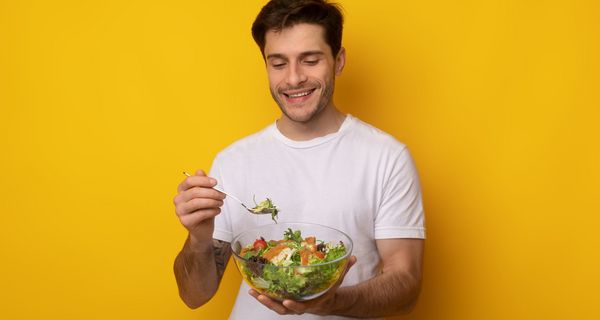 Ein Mann lächelt und hält eine Schüssel mit Salat und eine Gabel in der Hand.