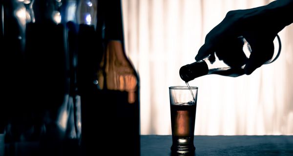 Hand hält eine Flasche mit Alkohol und schenkt in ein Glas ein.