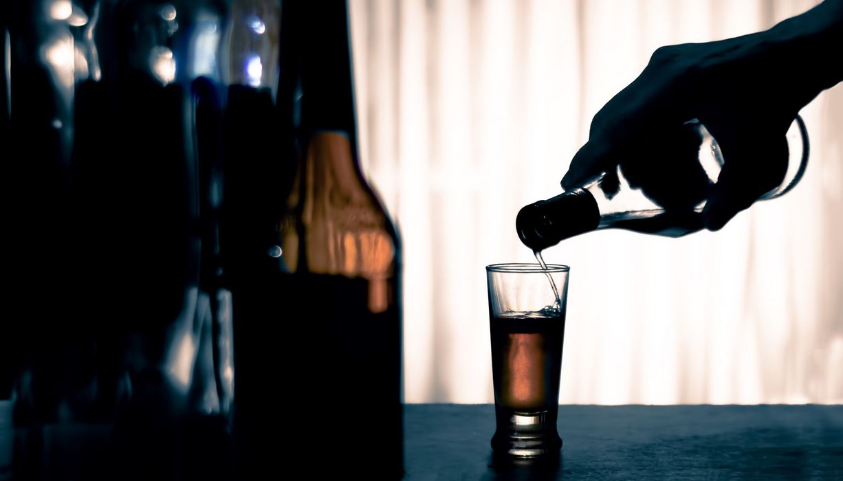 Hand hält eine Flasche mit Alkohol und schenkt in ein Glas ein.