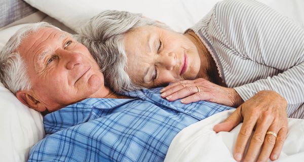 Ein Paar jenseits des 60. Lebensjahrs kuschelt im Bett.