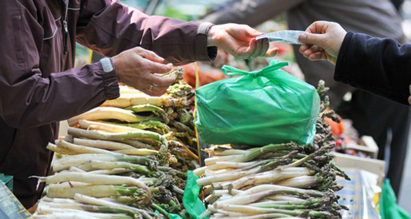 Markstand mit grünem Spargel, grüne Plastiktüte, Geld wird gezahlt von Käufer an Verkäufer, Köpfe sind nicht zu sehen