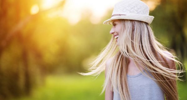 Junge Frau mit einem Hut schwingt ihre langen blonden Haare und lacht.