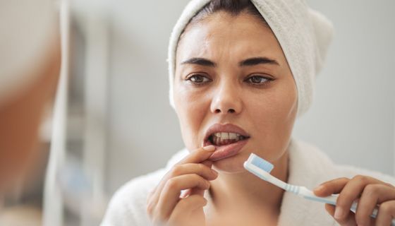 Frau schaut im Spiegel besorgt auf ihr gerötetes, blutendes Zahnfleisch.