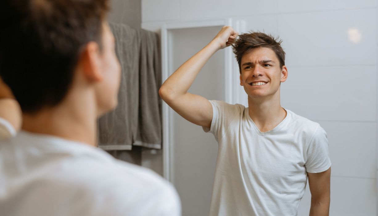 Junger Mann steht vor dem Spiegel und rauft sich die Haare.