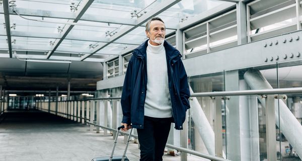 Älterer Mann mit Koffer am Flughafen.