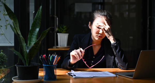 Junge Frau, sitzt am Schreibtisch und stützt ihren Kopf in die Hände.