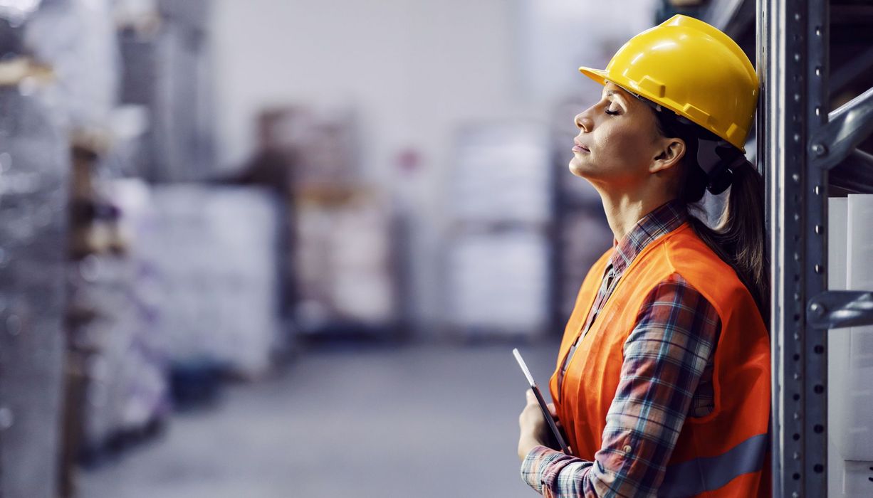 Frau auf der Baustelle, lehnt sich erschöpft gegen eine Wand.