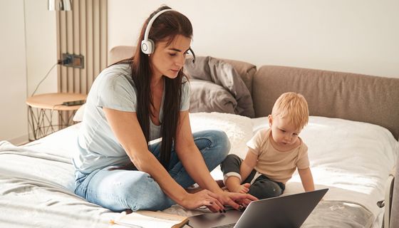 Frau am Laptop kümmert sich um ihr Kleinkind.
