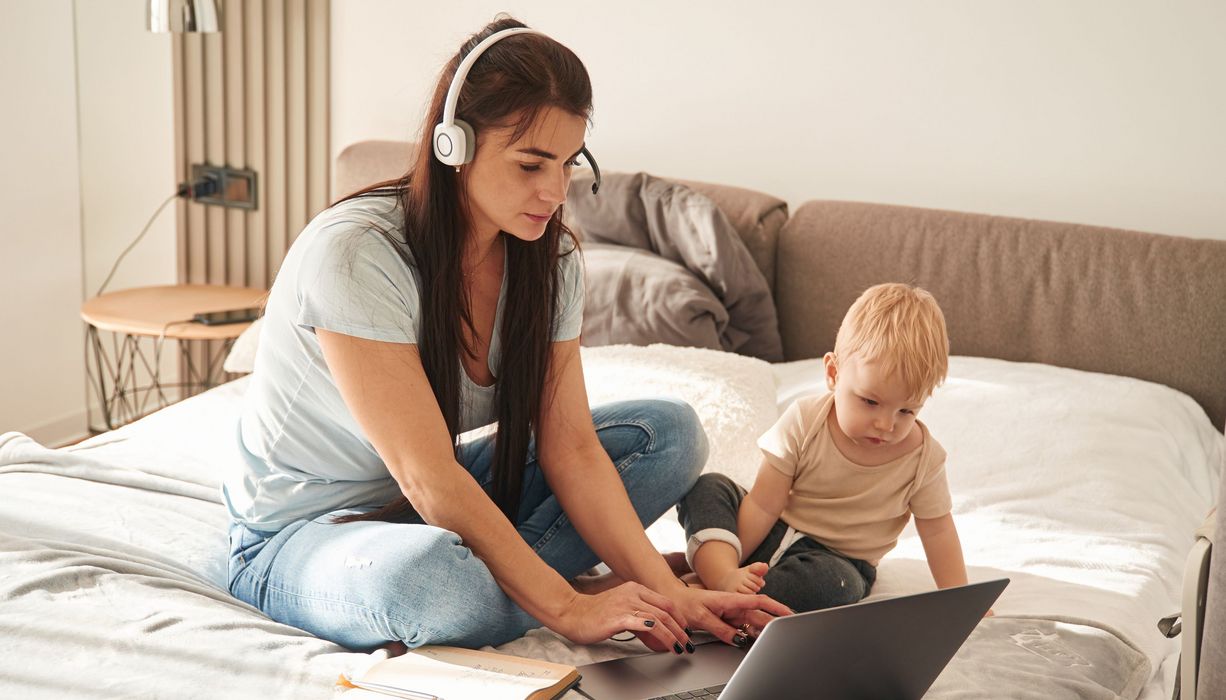 Frau am Laptop kümmert sich um ihr Kleinkind.