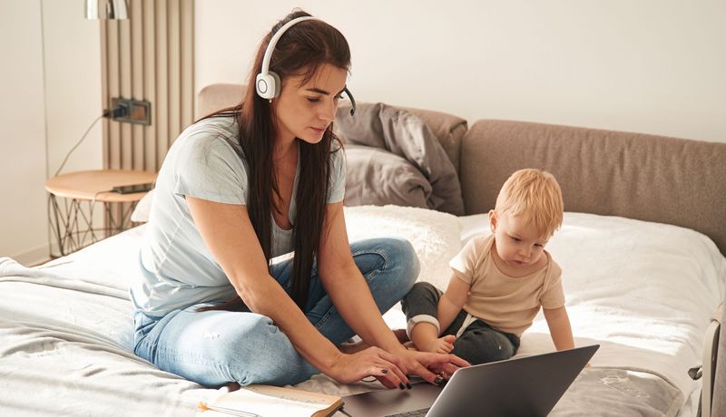 Frau am Laptop kümmert sich um ihr Kleinkind.