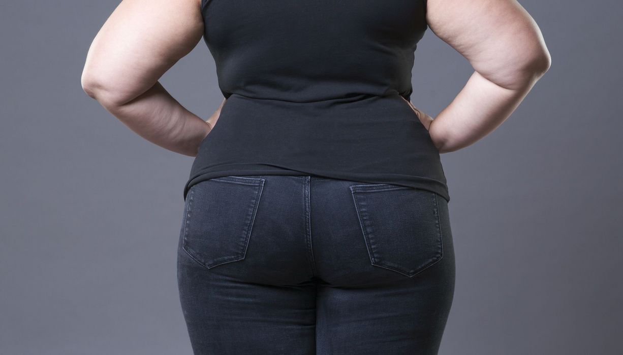 Das Gesäß einer mehrgewichtigen Frau ist von hinten zu sehen. Sie stützt ihre Arme in die Hüfte.