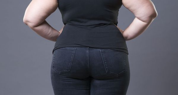 Das Gesäß einer mehrgewichtigen Frau ist von hinten zu sehen. Sie stützt ihre Arme in die Hüfte.