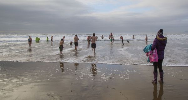 Menschen laufen am winterlichen Strand ins Wasser.