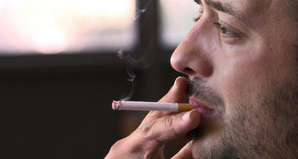 Mittelalter Mann mit Dreitagebart im Profil zieht an einer Zigarette