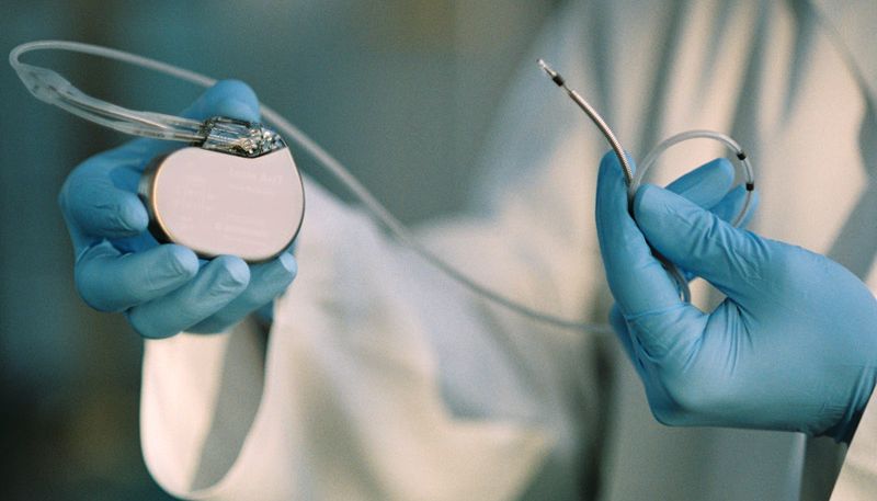 Implantierbarer Defibrillator, gehalten von Händen in blauen Gummihandschuhen