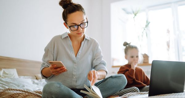 Frau mit Laptop auf dem Bett, neben ihr ihre Tochter.