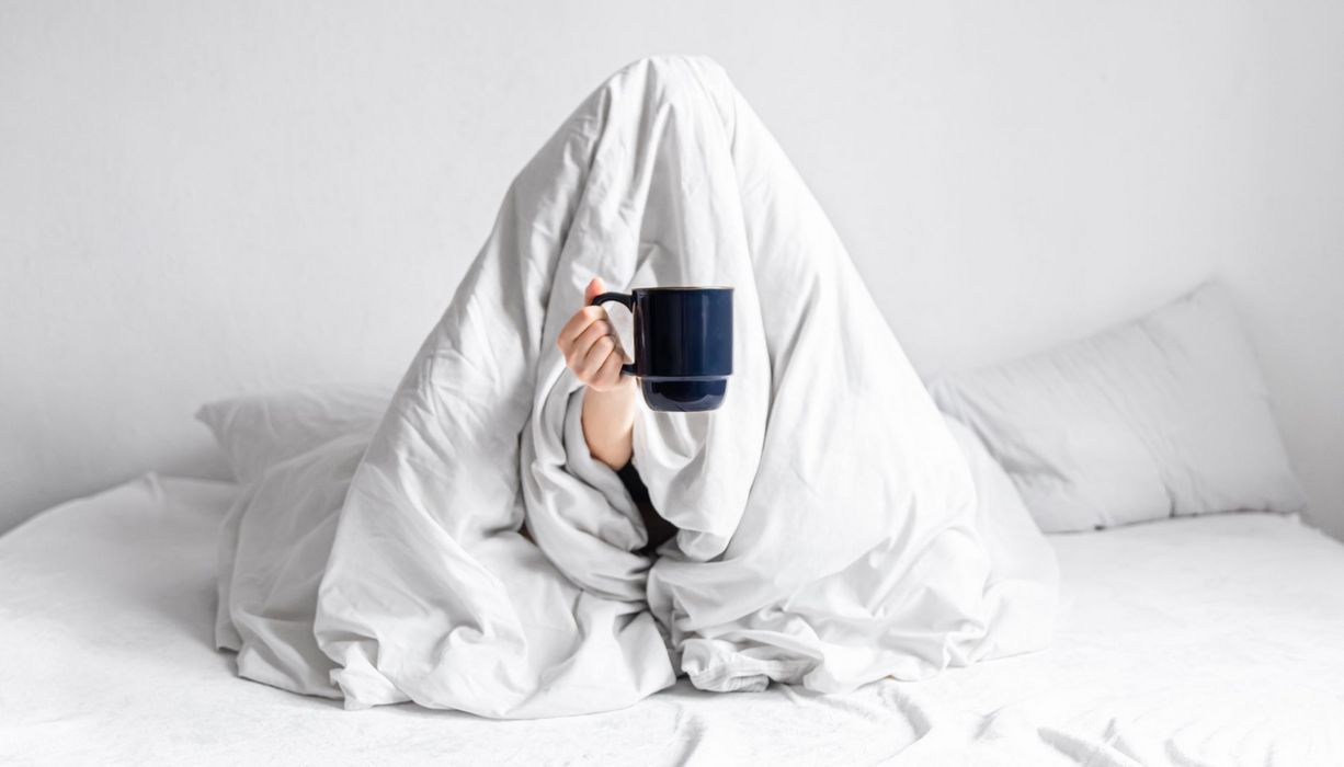 Mann oder Frau, haben eine Decke über dem Kopf und eine Tasse Kaffee in der Hand.