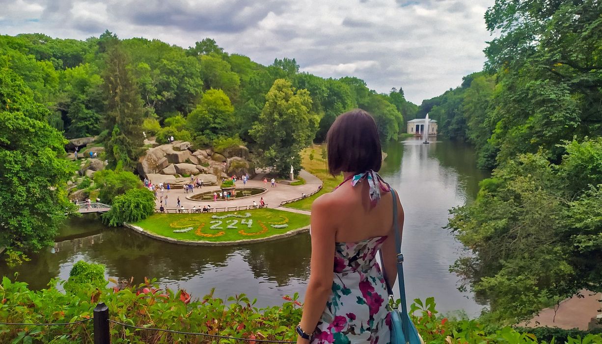 Frau, schaut herunter auf einen Park mit einem großen Teich.